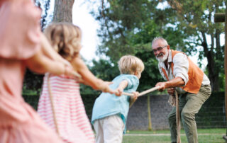 Grandfather has a tug of war with their grandkids. Fun games at family garden party.