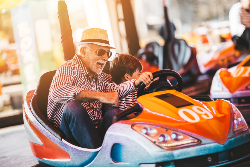 Grandfather and grandson having fun and spending good quality time together in amusement park. They enjoying and smiling while driving bumper car together.